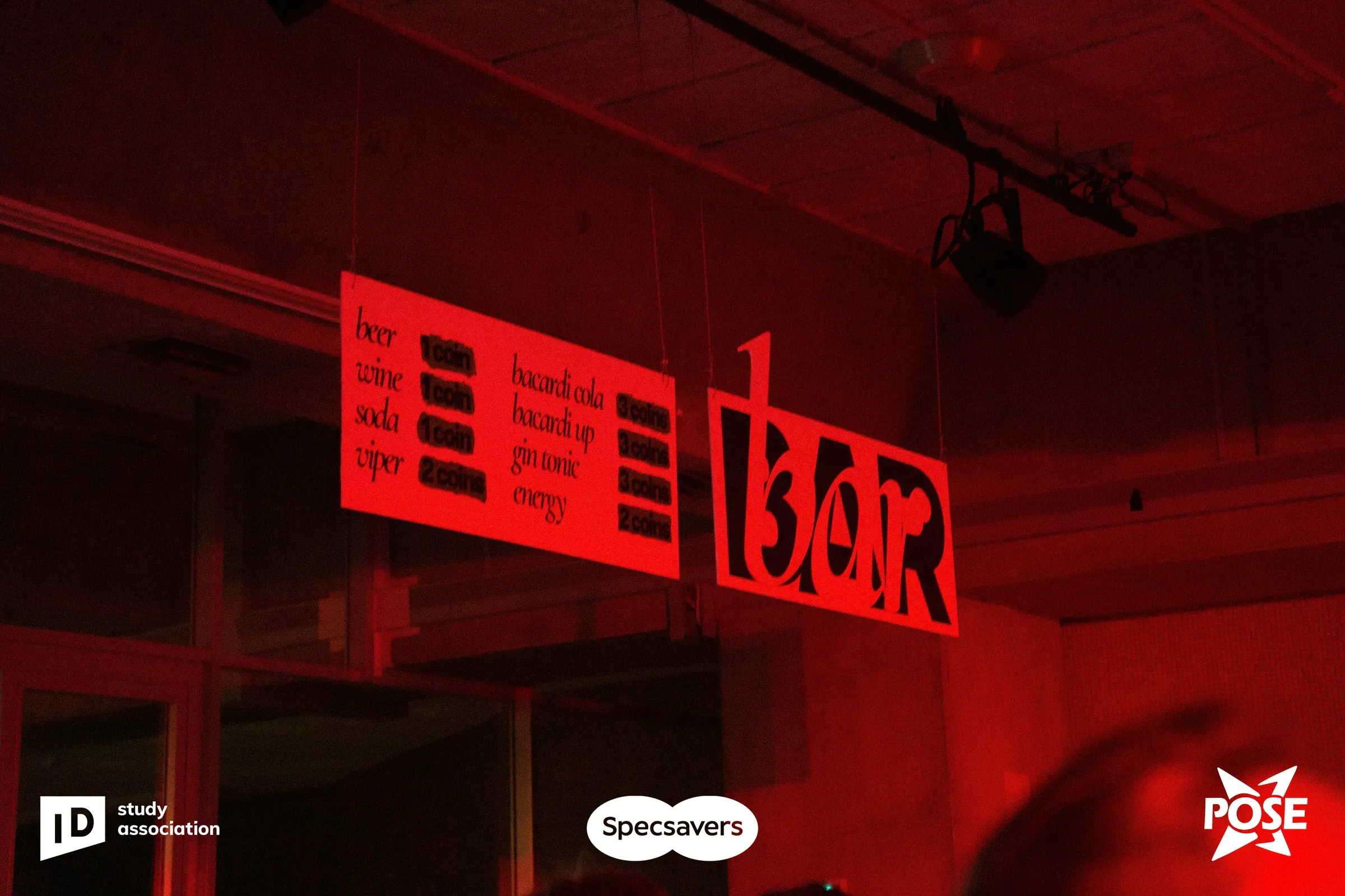 Red-lit bar with large cut-out signage and a price list in the festival style.