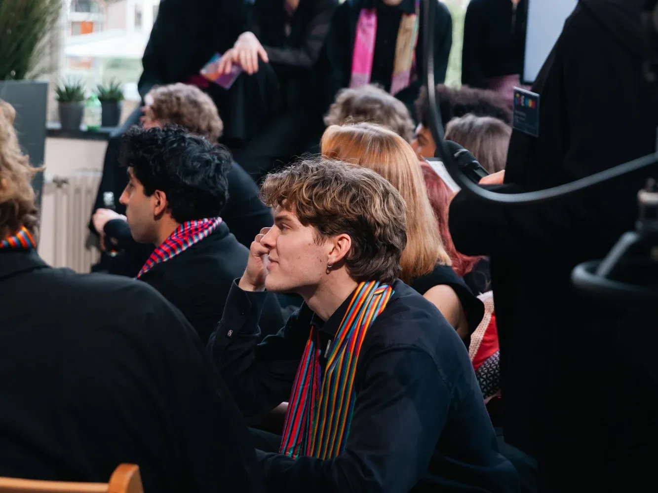 Team members at the final event wearing the striped Emergence scarves, with a film camera in the foreground.