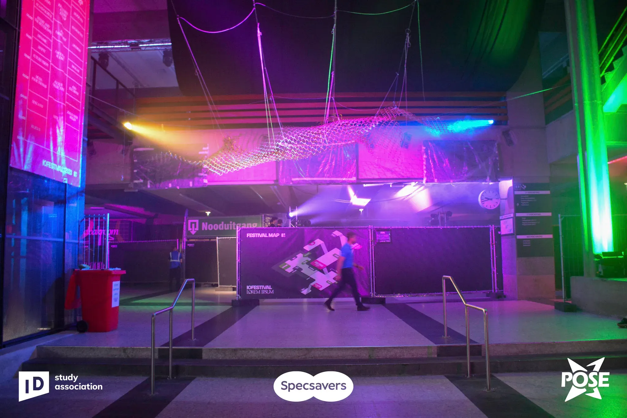 A dance floor lit in purple and green, with festival graphics projected on the back wall.