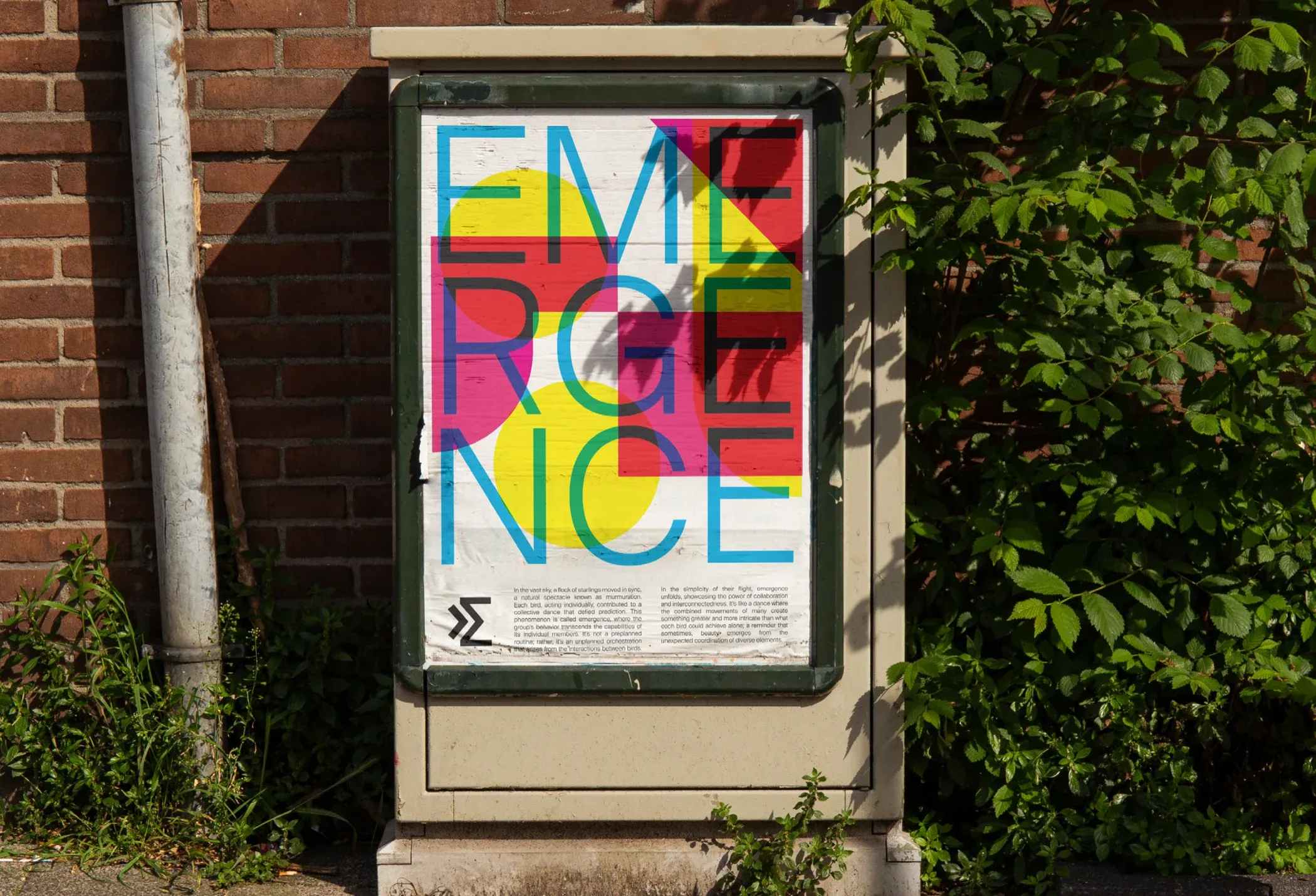 A poster in a frame on a utility box, with the word Emergence in large cyan letters over yellow and magenta shapes.