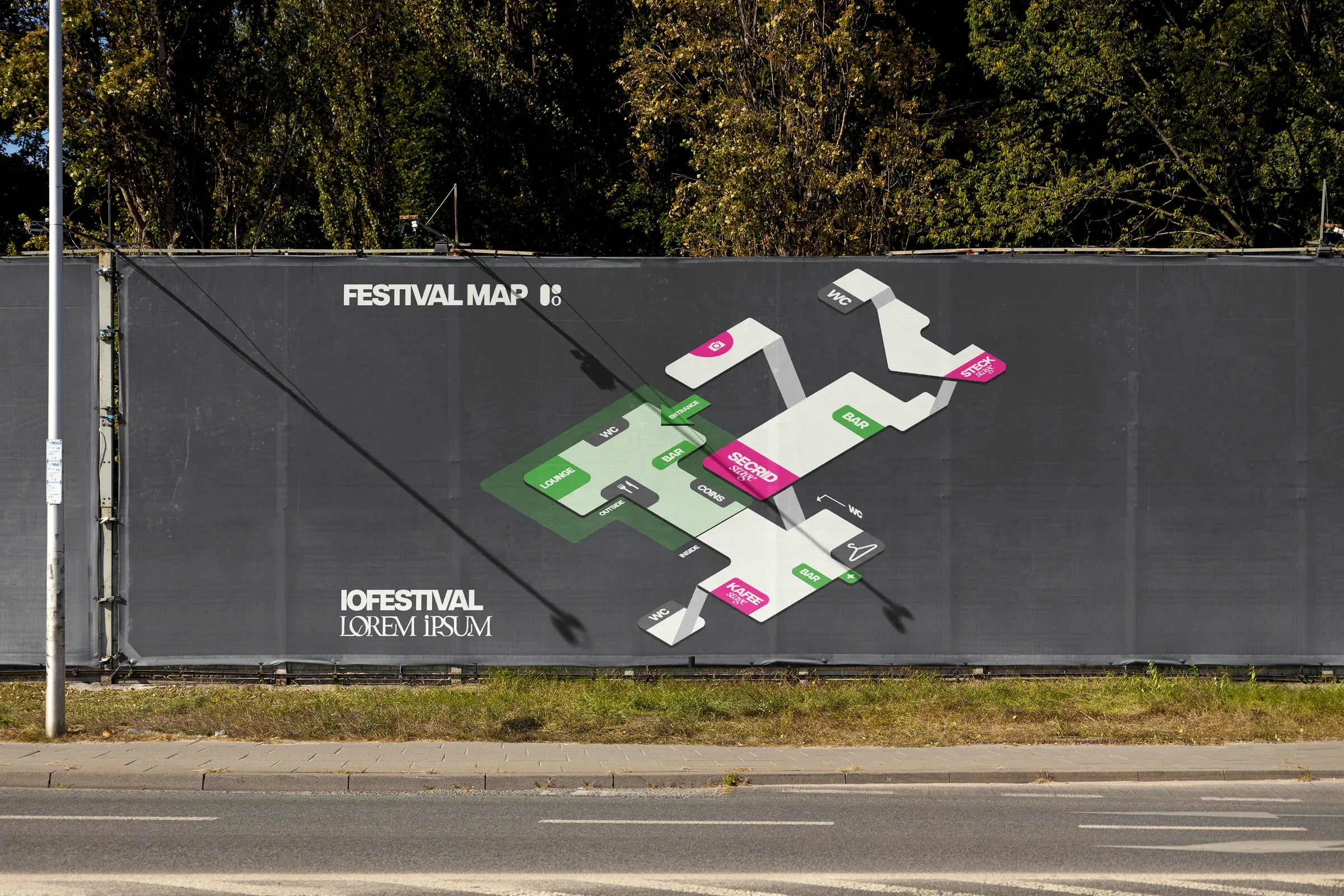 Large fence banner along a road showing an isometric festival map in white, pink and green on dark grey.