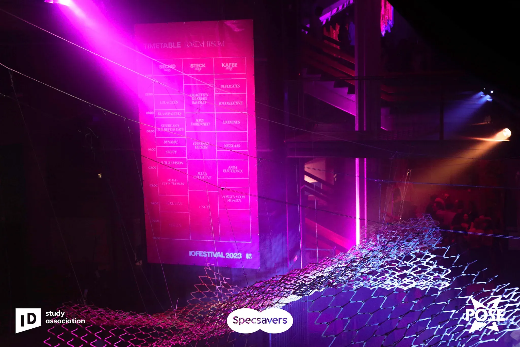 A pink-lit wall of text with a hanging net of lights in a dark hall.