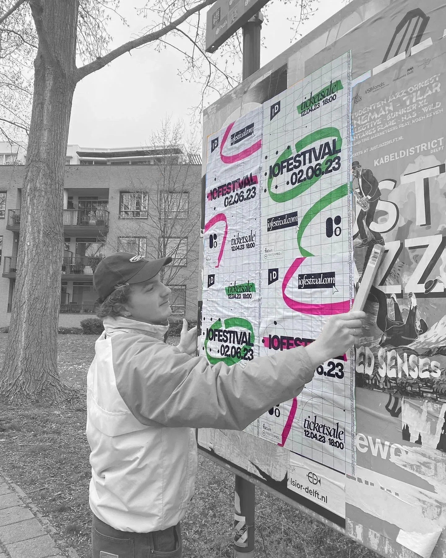 Black-and-white photo of a person pasting IO Festival posters onto an outdoor billboard.