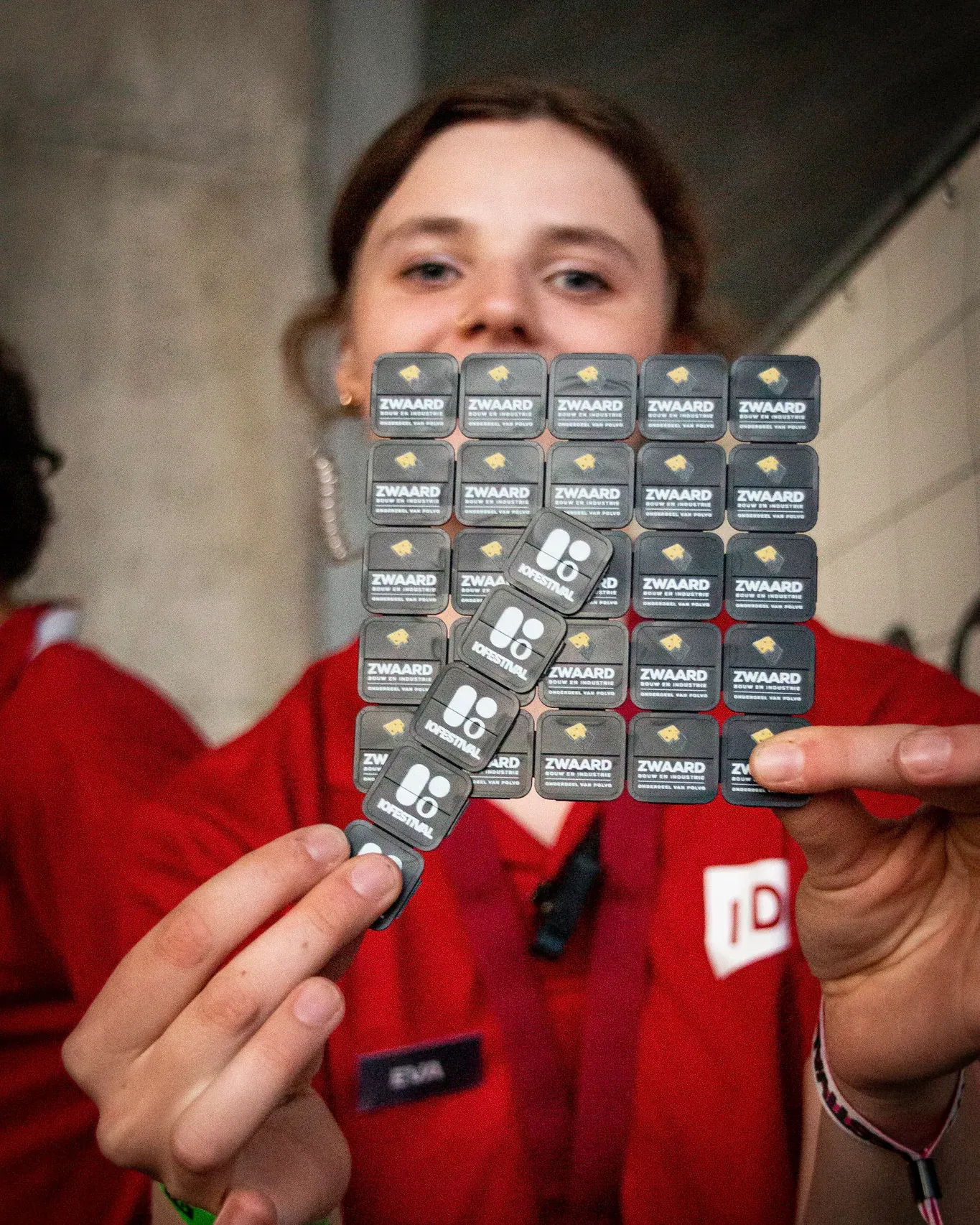 A crew member in a red shirt holding up a sheet of IO Festival wristbands towards the camera.